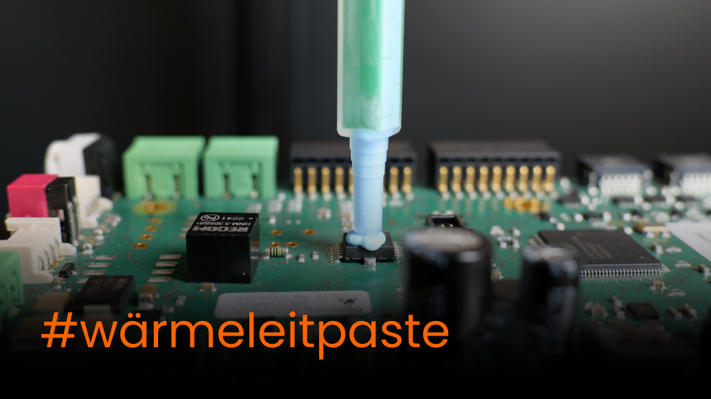 4 Nahaufnahme einer Platine, auf deren Prozessor Wärmeleitpaste mit einer Dosierspritze aufgetragen wird. Im Vordergrund steht der Schriftzug „#wärmeleitpaste“ in Orange.